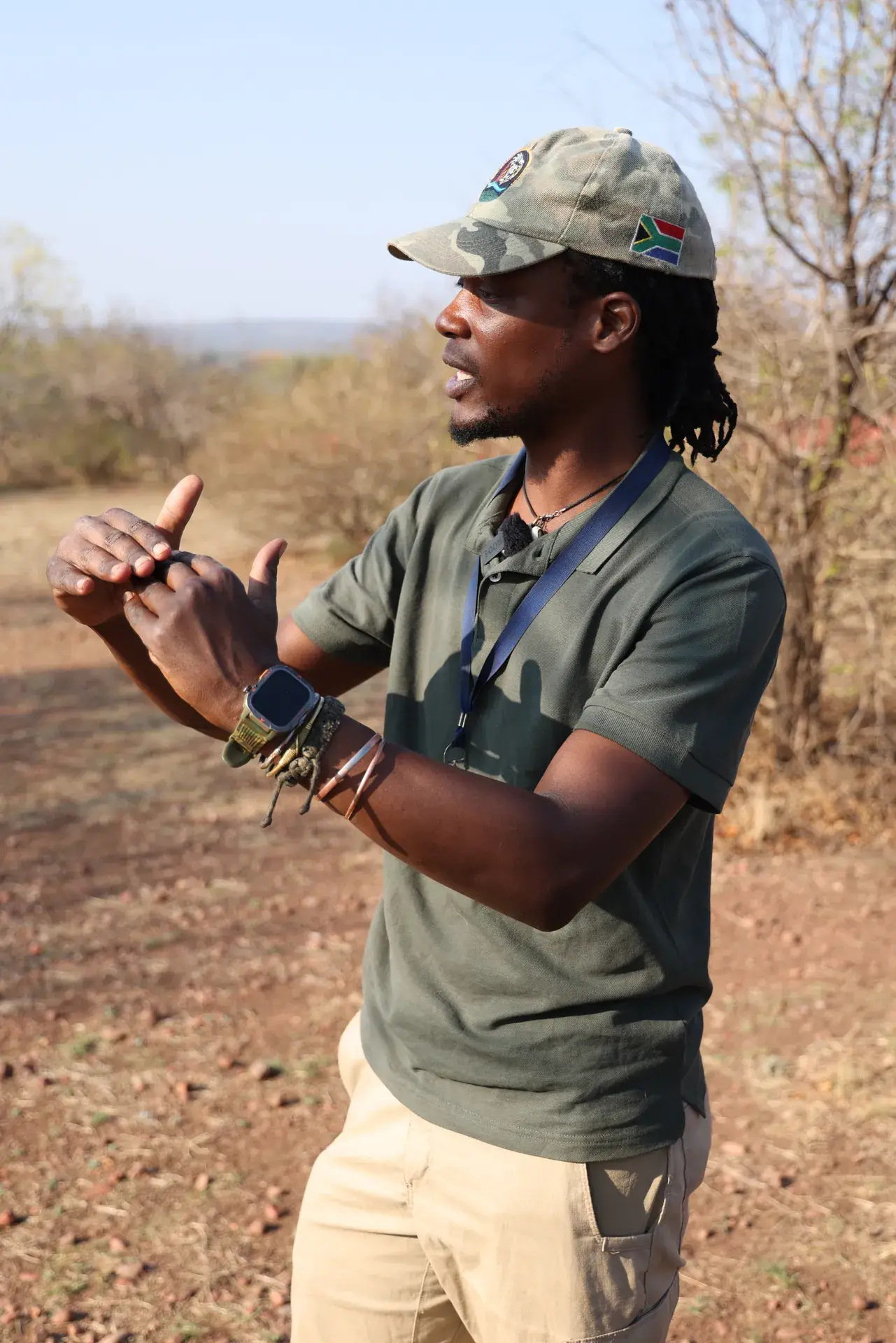 Guide in a green uniform standing among bushveld trees