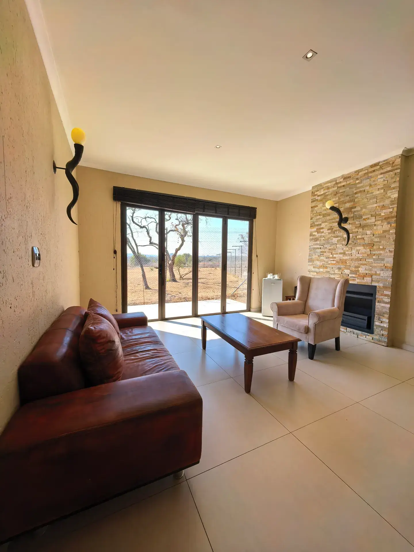 Lounge with leather sofas, a fireplace and doors opening to the bushveld